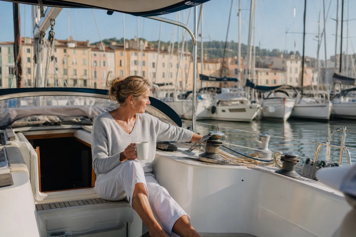 A boat-sitter with a coffee in the cockpit of a sailboat in a sunny marina, the hatch open to air the boat